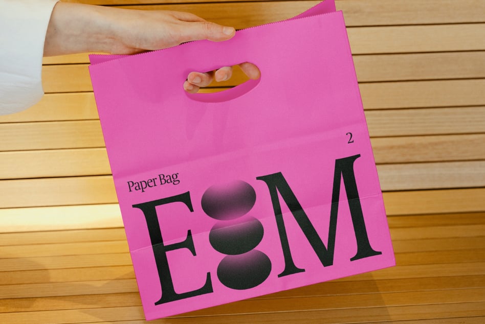 Hand holding magenta paper bag with shadowed black E8M on wooden deck