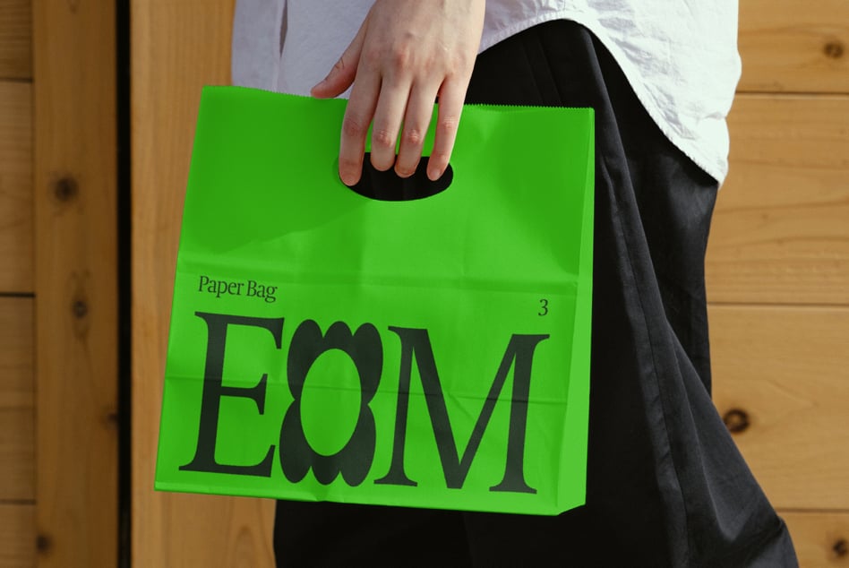 Bright green paper bag with black die-cut handle held in hands against wooden floor