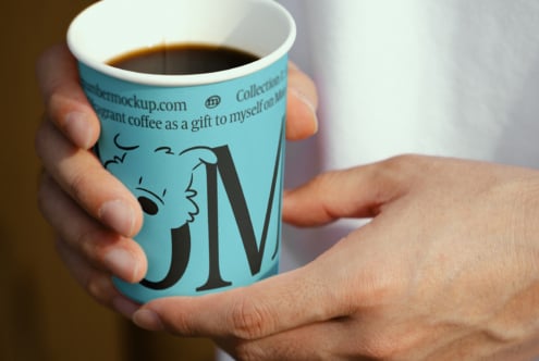 Hand holds a blue coffee cup with graphic design, showcasing elegant font and illustration perfect for branding mockups and product templates for designers.