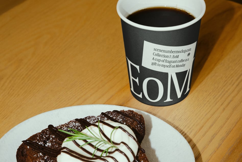 Black coffee cup with label next to chocolate cake on wooden table
