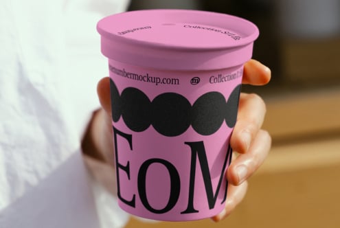 Hand holding a pink paper cup featuring bold typography and black design elements. Ideal for branding mockups, packaging design, and product presentation.