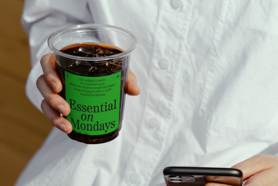 Hand holding clear cup mockup with neon green label over iced coffee drink