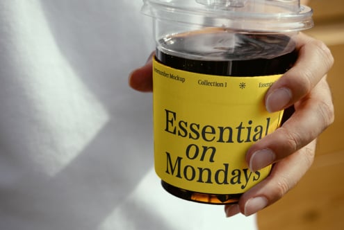 Hand holding a plastic cup with black coffee labeled Essential on Mondays Dreamumber Mockup Collection Fonts Templates Designers Digital Assets Creative