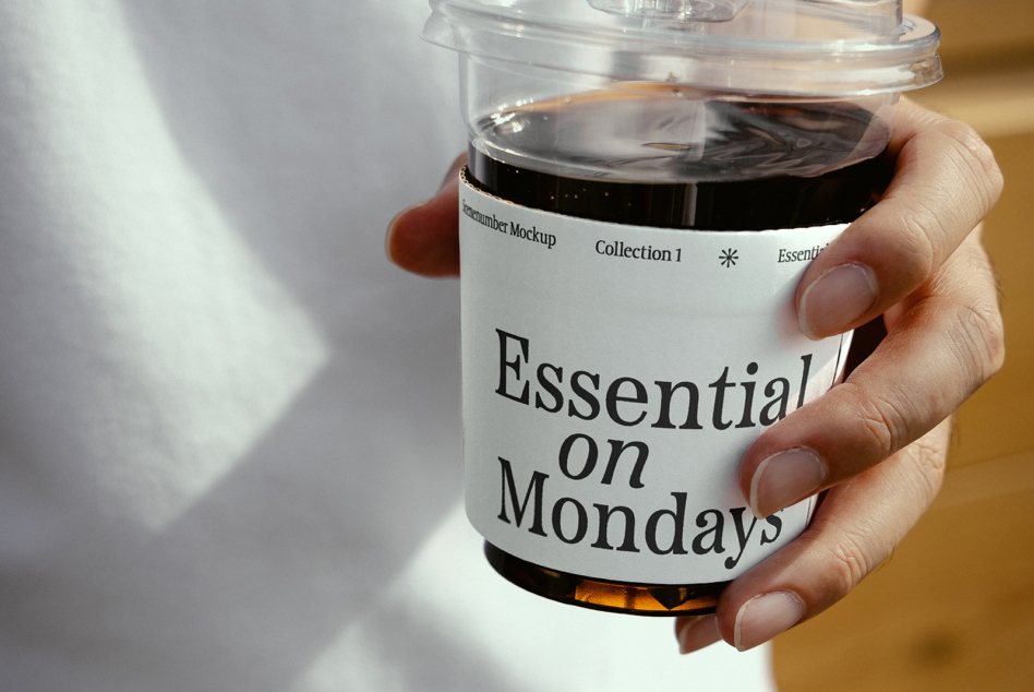 Close up of hand holding clear container with black liquid labeled Essential on Mondays