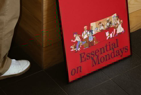Bold red poster featuring diverse characters with the text Essential on Mondays leaning against a wooden surface perfect for graphics and mockups