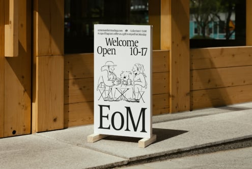 Mockup of a café sidewalk sign with minimal illustration. Text reads Welcome Open 10-17. Wood background. Perfect for graphic design projects.