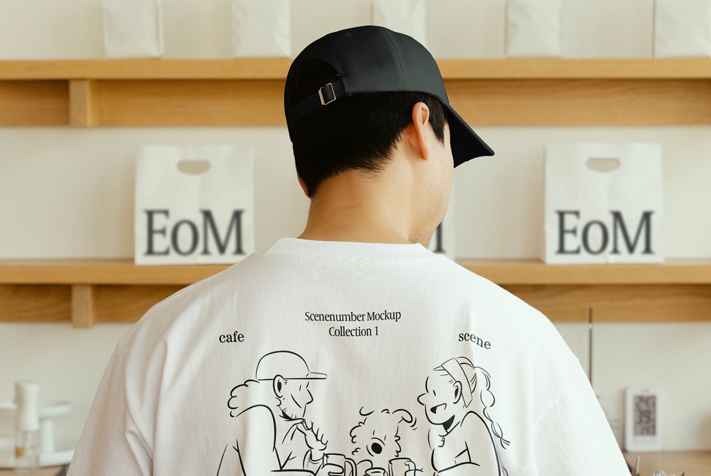 Man in black cap wearing white T-shirt with cartoon design stands in front of shelves. Ideal for mockup display, apparel showcase, graphic design.