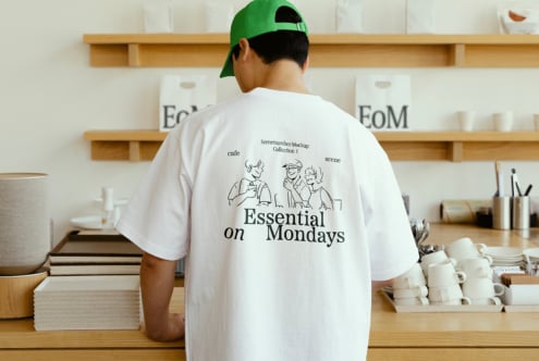 Man in green cap wearing white t-shirt with Essential on Mondays text and illustration in cozy cafe setting perfect for mockup or design template resource