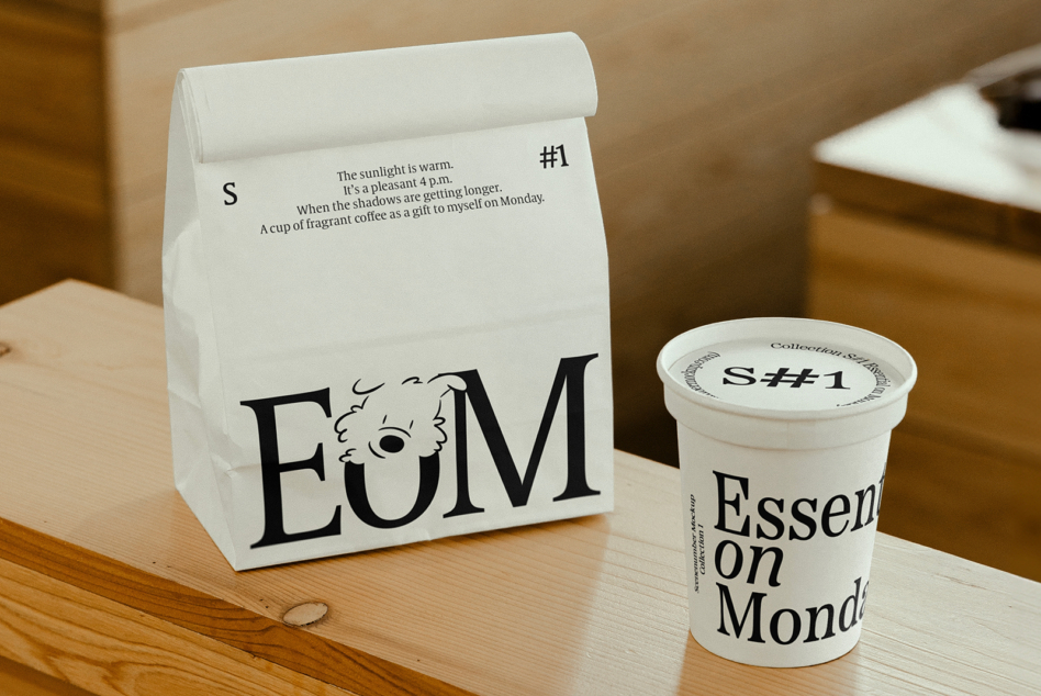 White paper bag with EOM branding next to matching coffee cup on wooden table