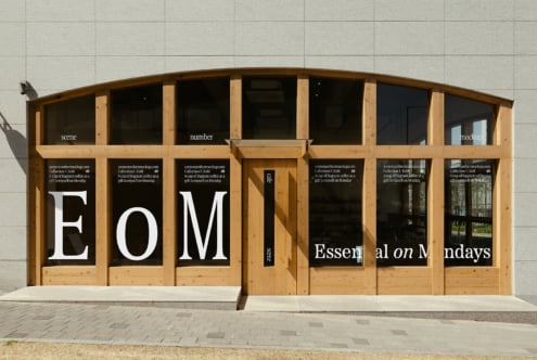 Storefront mockup with wooden frame and large glass windows displaying bold text Essential on Mondays. Perfect for designers seeking realistic scenes.