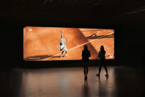 Large indoor display showcasing tennis player on clay court with two people viewing. Ideal for mockups and digital assets in sports design projects.