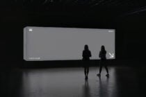 Gray blank billboard display in dark warehouse space with silhouettes