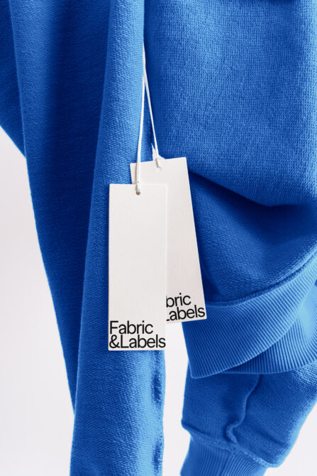 Folded blue fabric sweatshirts with dual white hang tag labels mockup