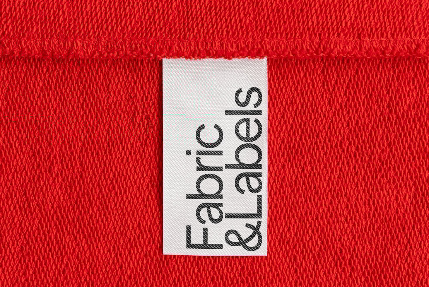 Red textile backdrop with a white fabric label reading Fabric & Labels, perfect for mockups, branding and textile design. Textural design asset for designers.