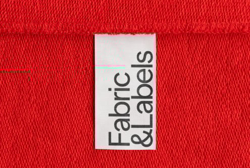 Red textile backdrop with a white fabric label reading Fabric & Labels, perfect for mockups, branding and textile design. Textural design asset for designers.