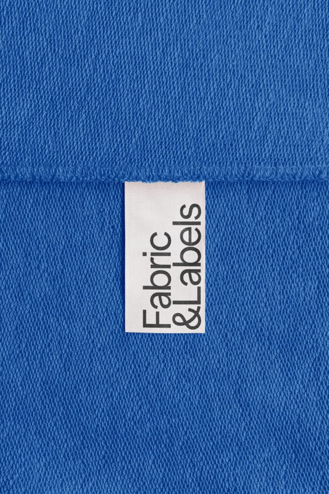Blue fabric texture with a white clothing label displaying Fabric Labels. Ideal for apparel design templates, textile mockups, and branding graphics.