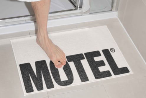 Person stepping on white doormat with black MOTEL text in entryway