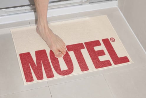 Toes on cream motel doormat with red text at bathroom doorway