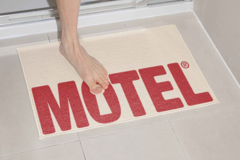 Toes on cream motel doormat with red text at bathroom doorway