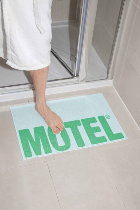 Foot on light blue motel entry mat with green lettering by shower