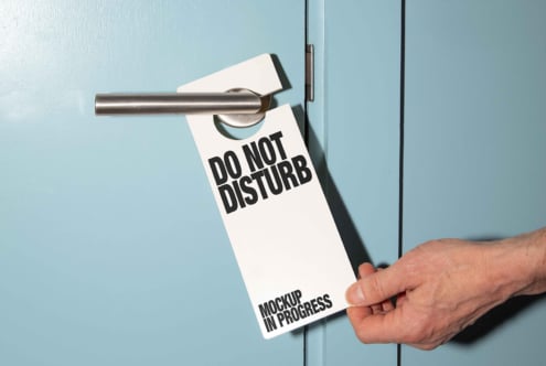 Mockup of a door hanger reading Do Not Disturb held by a hand on a blue door. Perfect for hotel signage designs and print templates for designers.