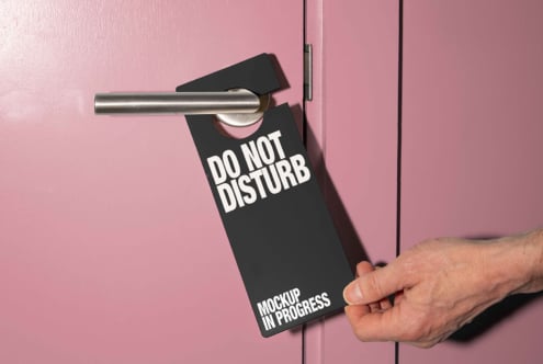 Pink door with silver handle displaying a black Do Not Disturb door hanger mockup. Perfect for designer templates and hotel graphics.
