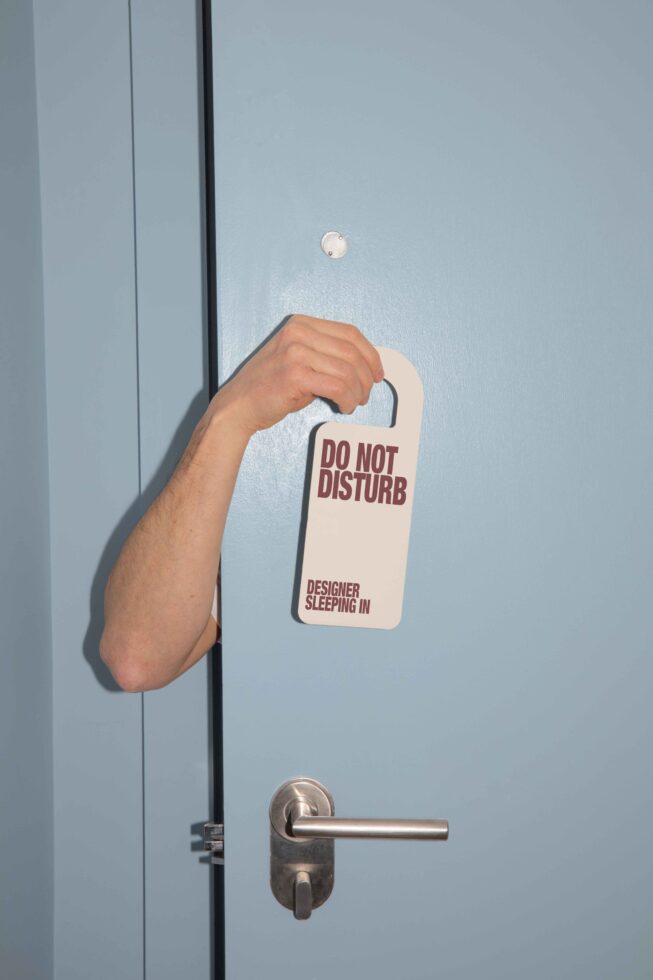 Arm holding do not disturb sign in a blue door for designer humor mockup graphic. Perfect for creative workspace templates and playful designs.