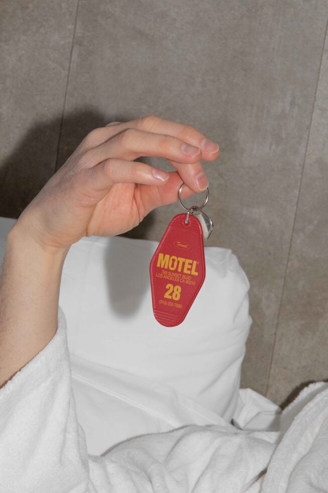 Hand holding a red motel keychain with room number 28 against a white bed backdrop. Perfect for mockups, travel-themed graphics, and design projects.