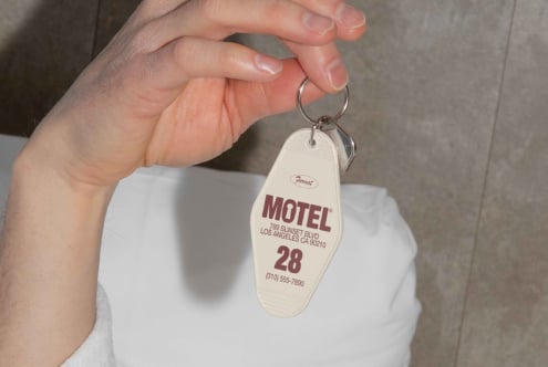 A hand holds a retro motel key tag with text Motel Los Angeles 789 Sunset Blvd. Vintage design perfect for graphic projects or mockup templates.