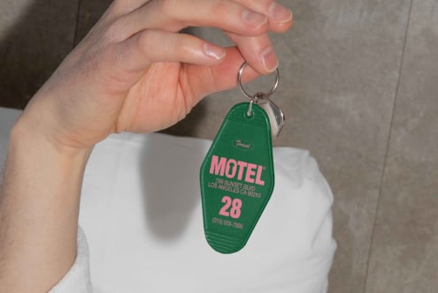 Hand holding a green vintage motel keychain with pink text for room 28 Los Angeles. Perfect for retro mockups or graphic design resources.