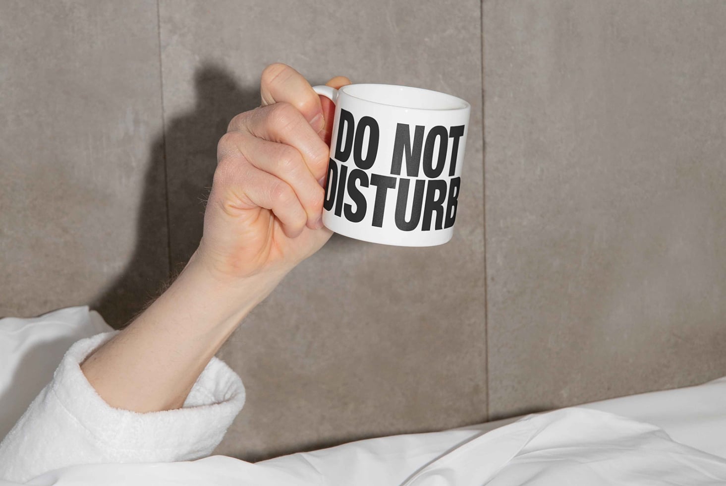 Hand holding white mug with do not disturb text against gray wall