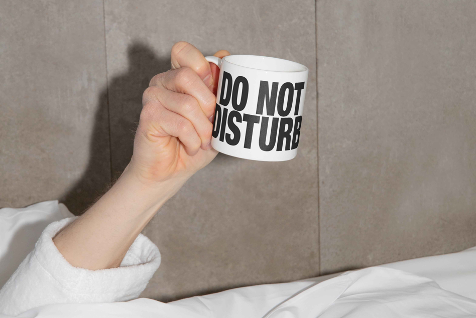 Hand holding white mug with do not disturb text against gray wall