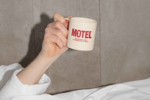 Hand holding mug with Motel branding in cozy setting. Perfect for mockups or template designs. Neutral background. Ideal for designers seeking graphics.
