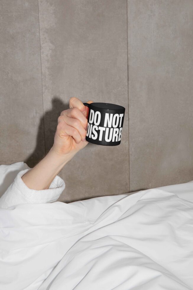 Hand holding black mug with do not disturb text on gray bedding