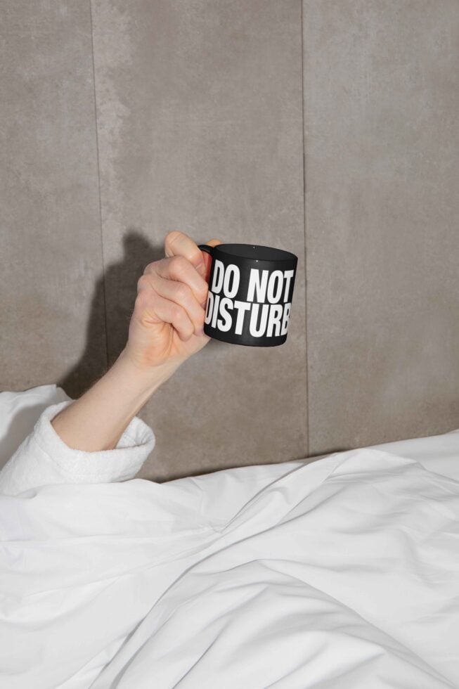 Hand holding black mug with do not disturb text on gray bedding