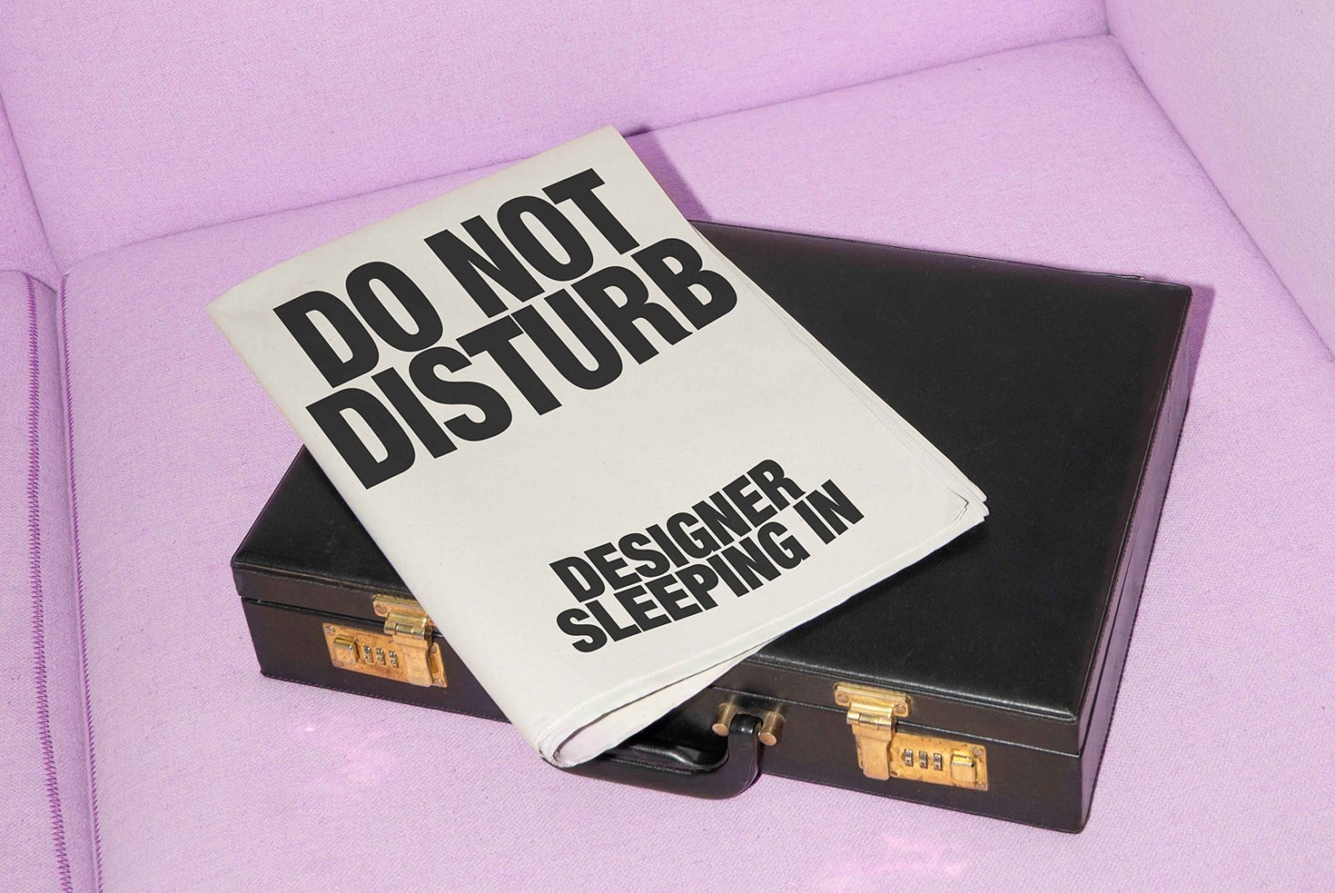 Black briefcase with newspaper headline Do Not Disturb Designer Sleeping In on pink fabric background mockup design typography SEO digital asset