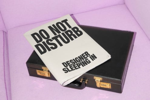 Black briefcase with newspaper headline Do Not Disturb Designer Sleeping In on pink fabric background mockup design typography SEO digital asset