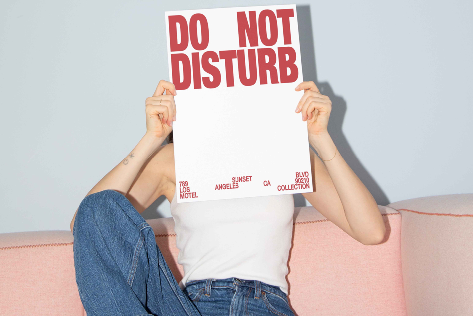 Person on pink couch holding red Do Not Disturb sign with address