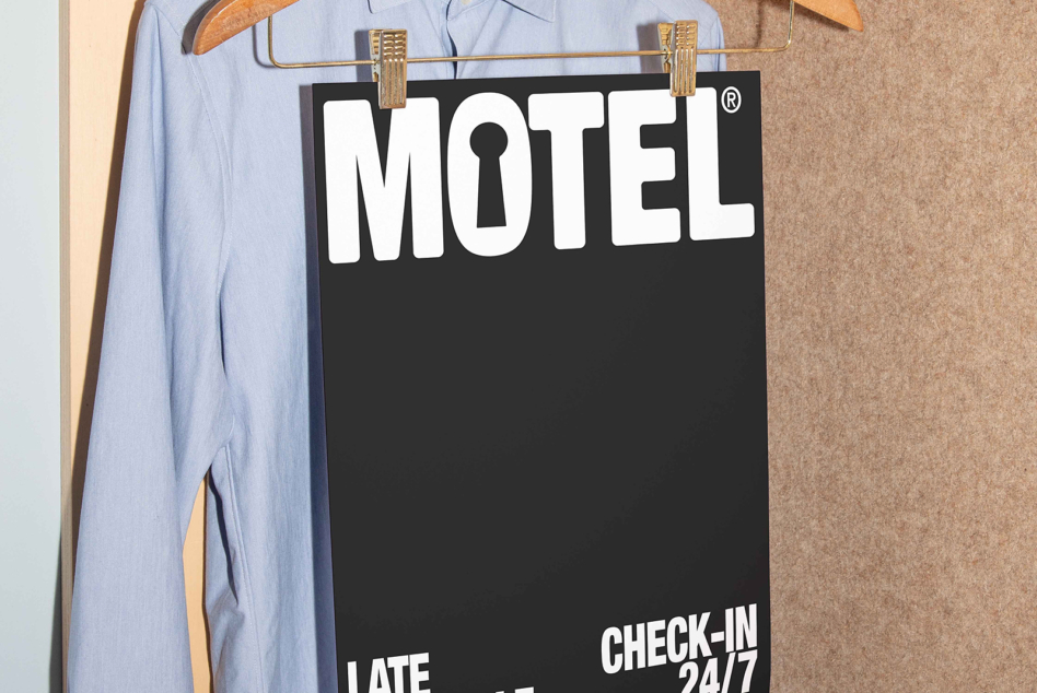 Black motel door hanger with white text clipped to wooden clothing hanger