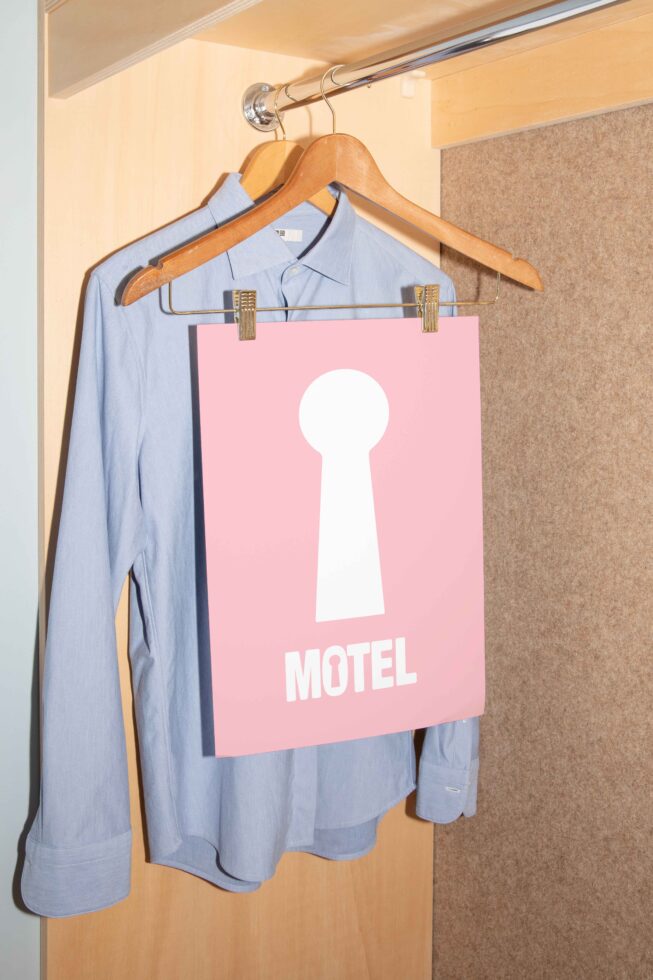 Blue shirt on hanger in closet with pink keyhole design graphic poster labeled Motel. Perfect for modern template mockups. Ideal for designers.