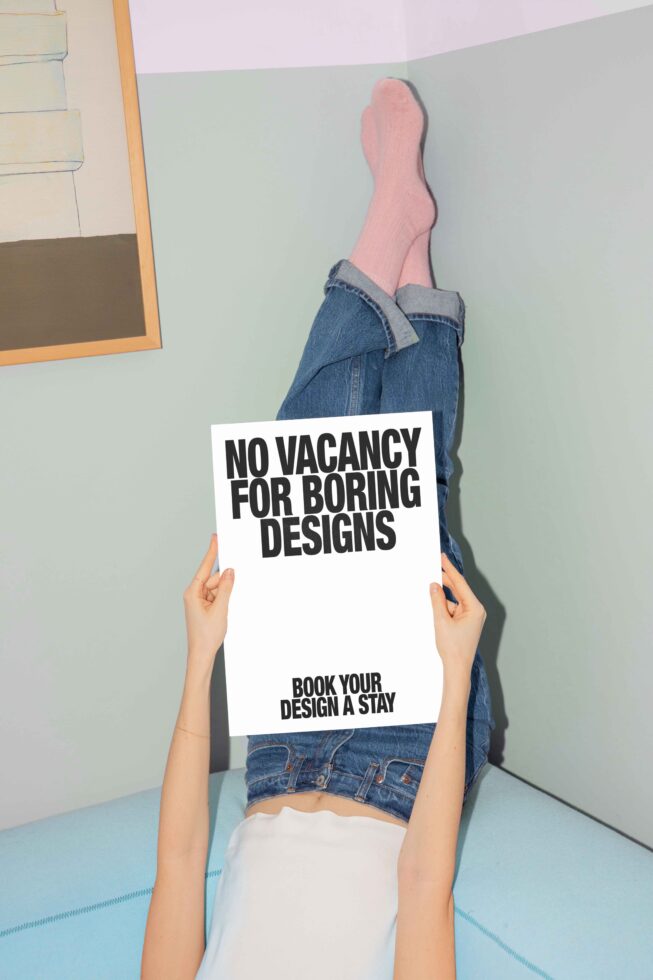 Designer holding a sign with No Vacancy For Boring Designs text. Minimalistic setting with pastel tones, focus on creativity, inspiration, unique design ideas.