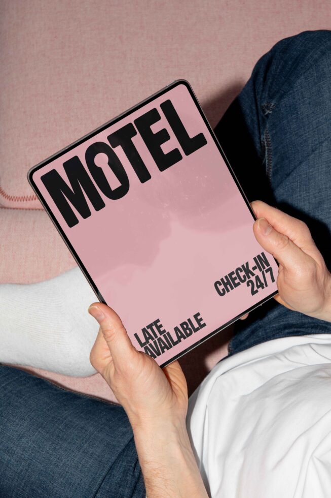 Tablet mockup featuring minimalist motel sign design in bold black font on pink background held by a person, ideal for branding and marketing.
