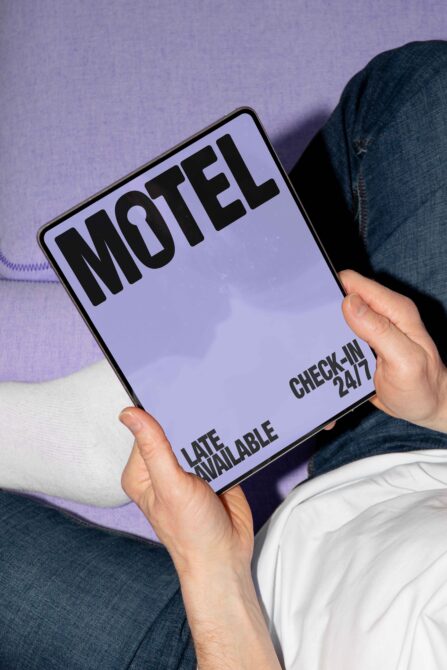 Person holding a digital tablet displaying a motel sign with bold black letters on a lavender background. Perfect for mockup showcasing fonts templates.