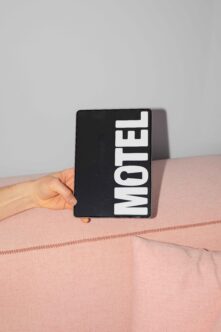 Black card held up displaying Motel text in white rotated typography