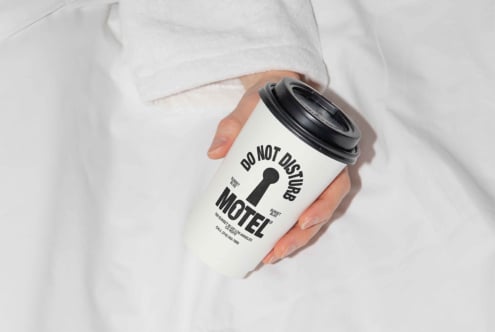 Mockup of a hand holding a paper coffee cup with do not disturb motel branding on a white background ideal for designers' templates and graphics projects
