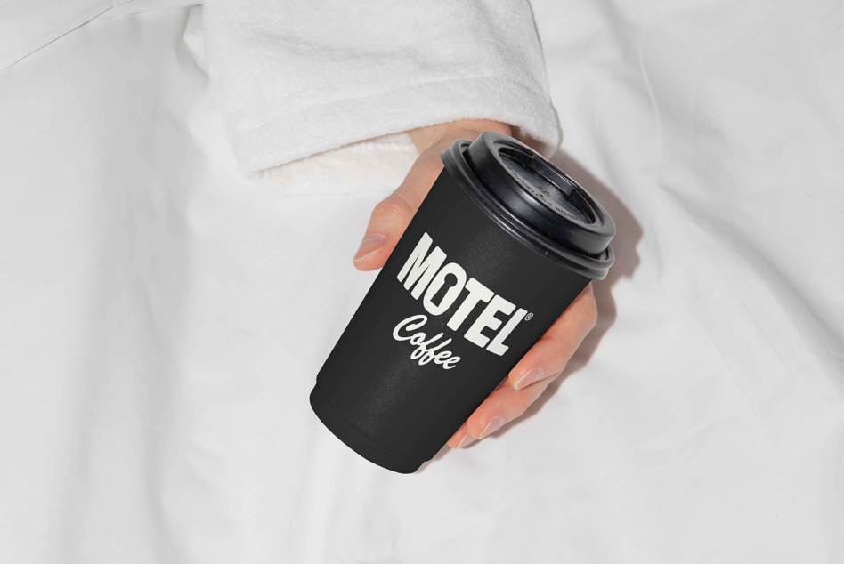Hand holding black Motel Coffee branded takeaway cup