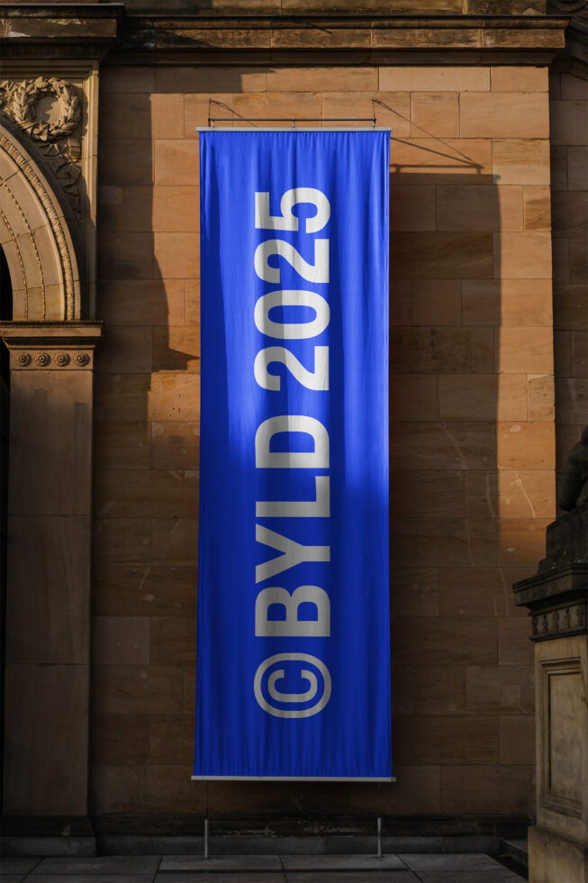 Vertical blue banner with bold letters BYLD 2025 set against a stone wall, ideal for architectural mockup presentations, outdoor signage, and urban design.