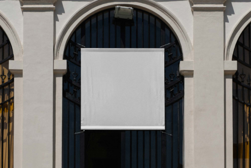 Blank white canvas banner suspended on ornate building entrance with dark doors