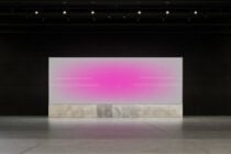 Large display screen with pink gradient on concrete stage floor under studio lights