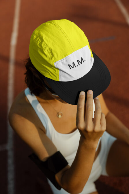 Close-up of person in athletic wear adjusting a yellow and white cap labeled MM on a sports track. Ideal for mockups and digital designs.